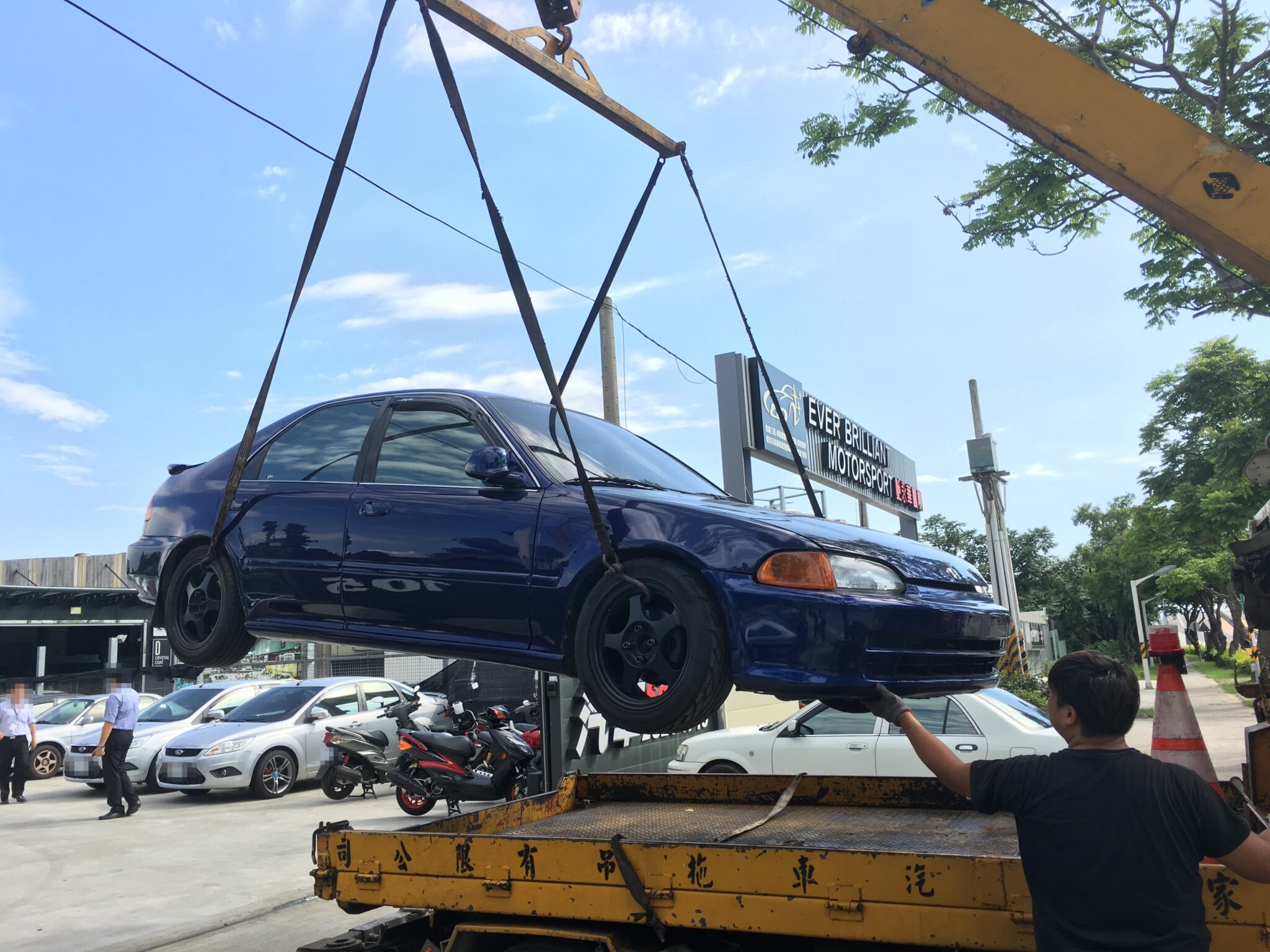 一台深藍色轎車被吊車吊起準備放上拖板車，示意車輛報廢回收的載運過程